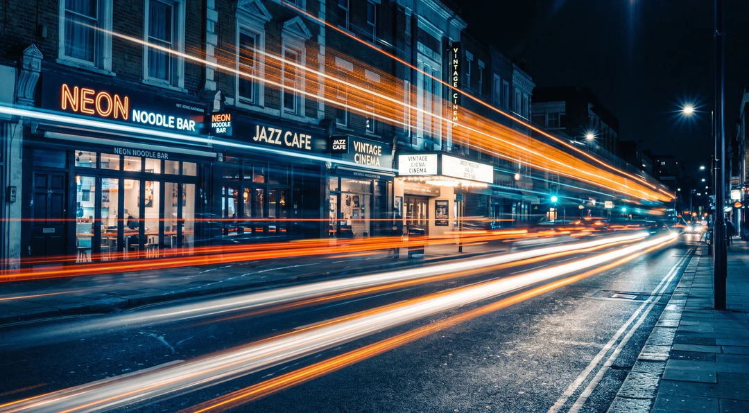 Long exposure of a city street at night with orange and white light trails.